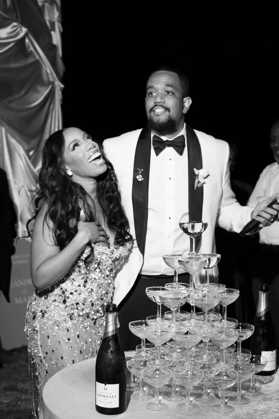 Couple riant devant une tour de coupes de champagne, de nuit