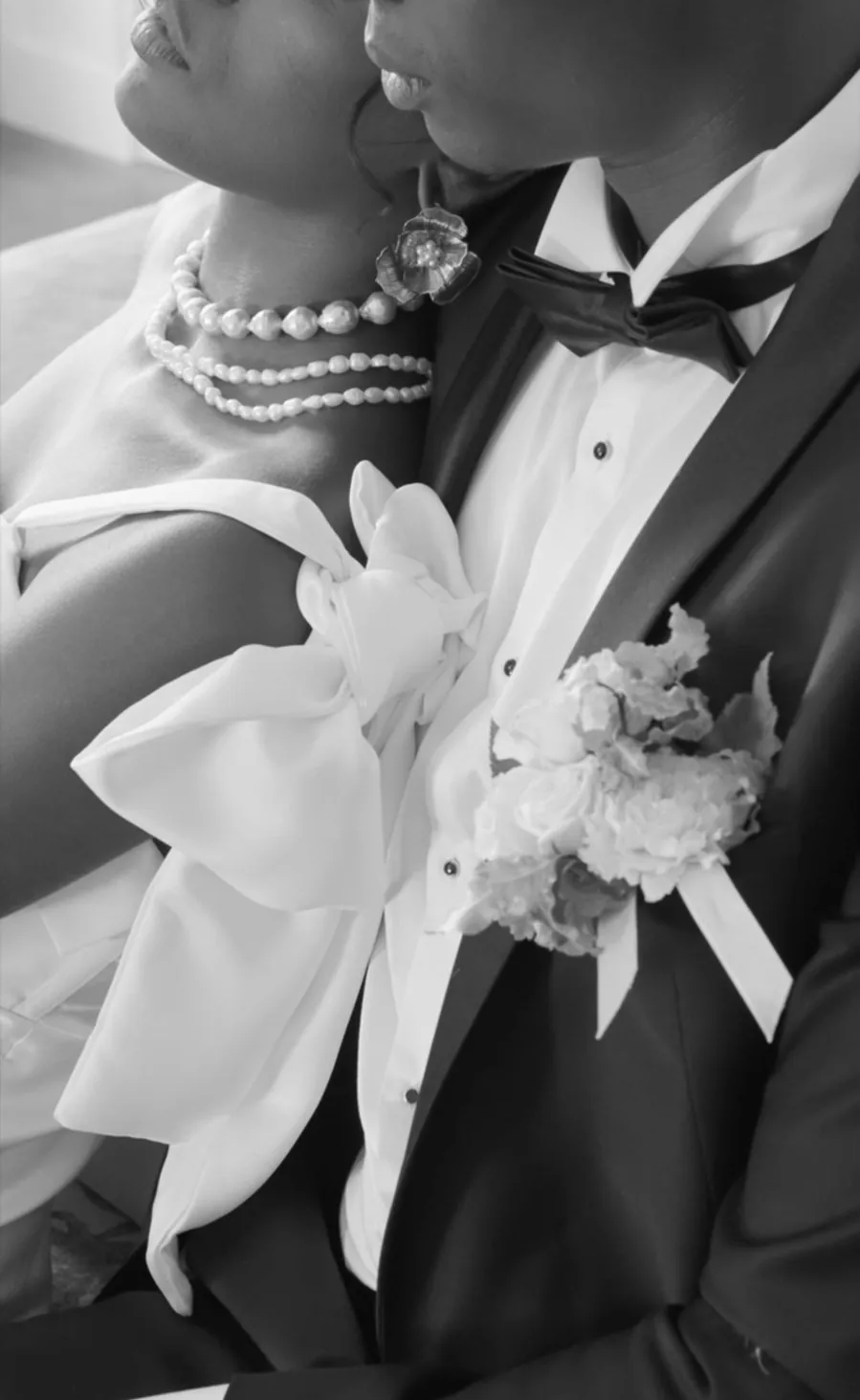 Détail en noir et blanc : collier de perles, nœud de la mariée et nœud papillon du marié