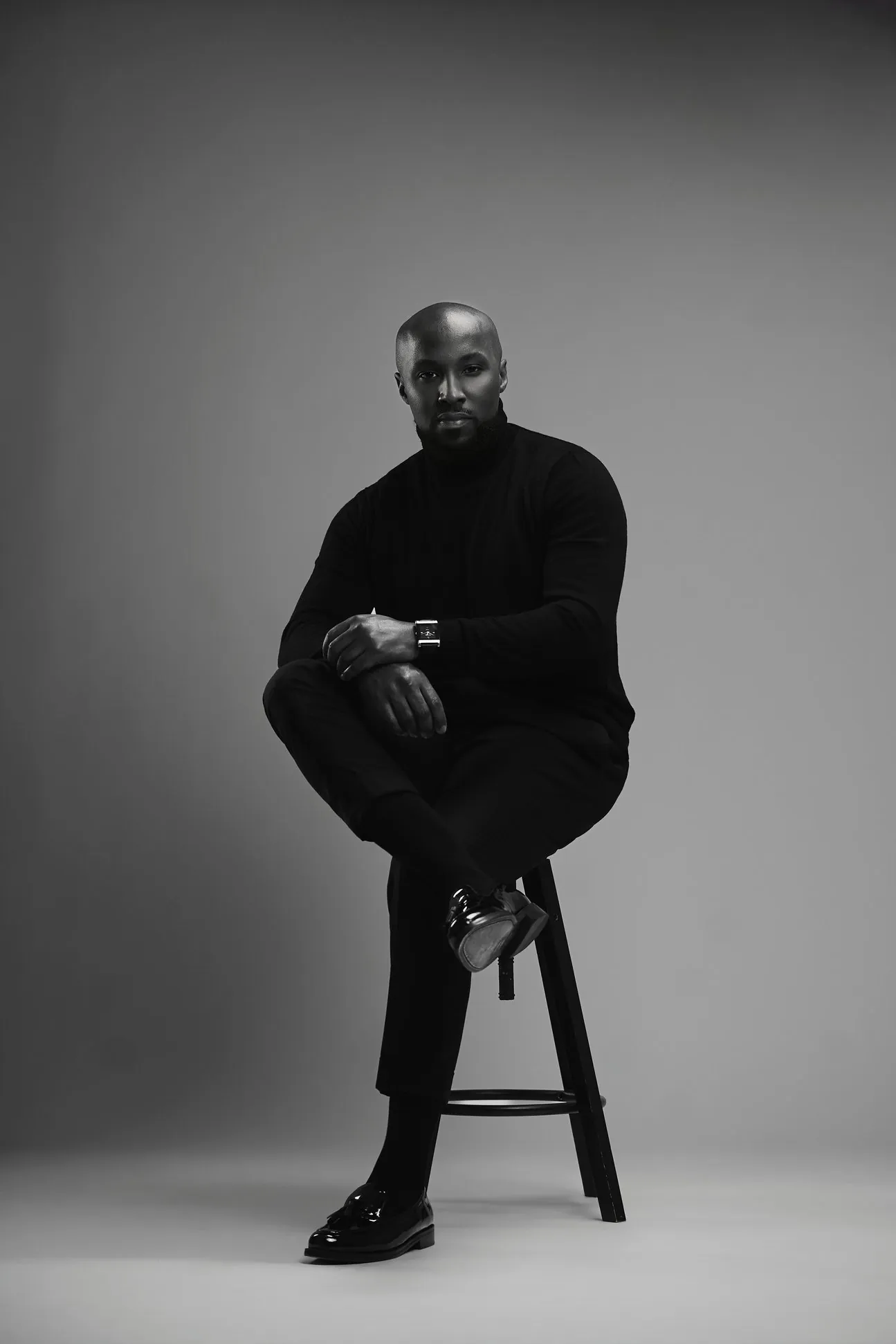 Portrait de Angelo Moreira, assis sur un tabouret, en noir et blanc