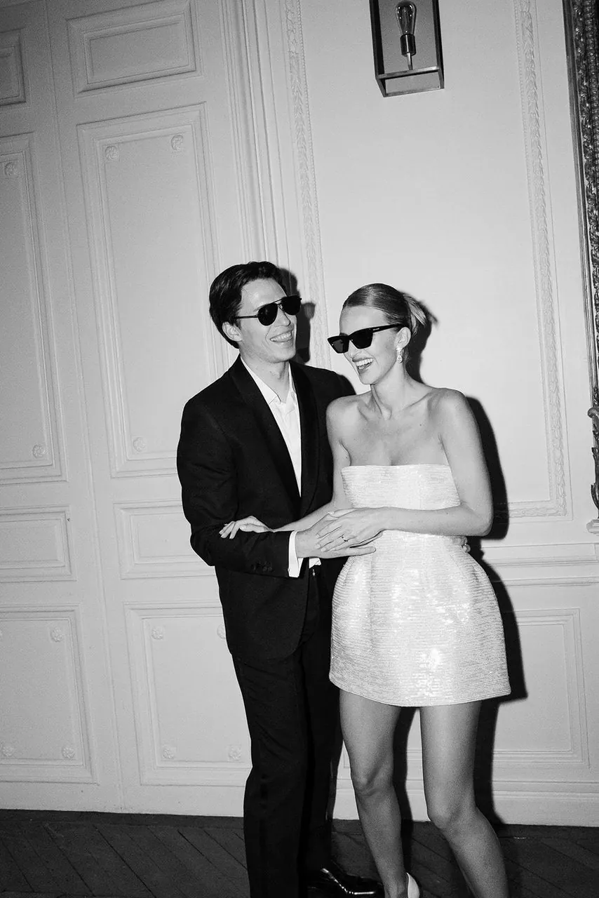 Couple enlacé en lunettes de soleil devant des boiseries blanches, en noir et blanc